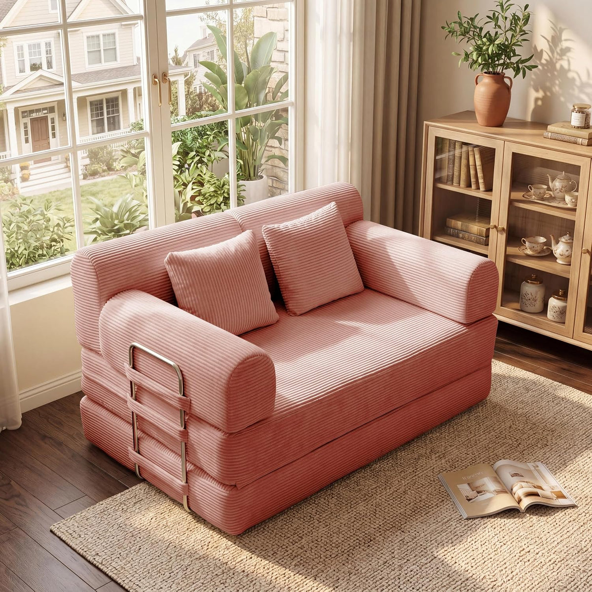 Pink ribbed loveseat with two matching throw pillows, metal side ladder, and an open magazine on the rug nearby.