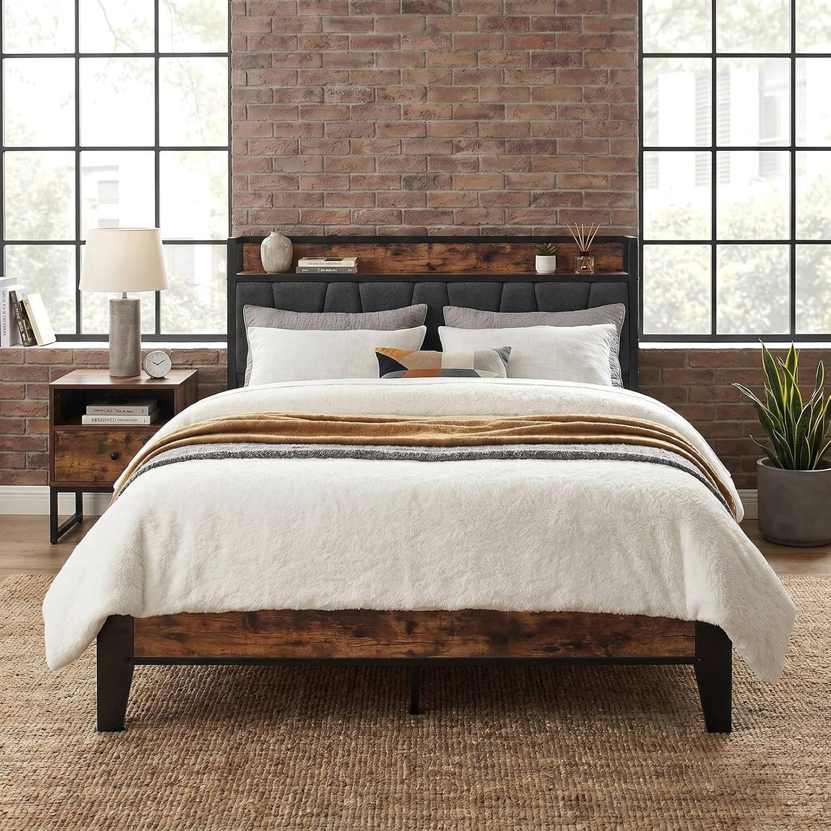 Straight-on view of a dark gray upholstered headboard with rustic wood shelf against a brick wall.