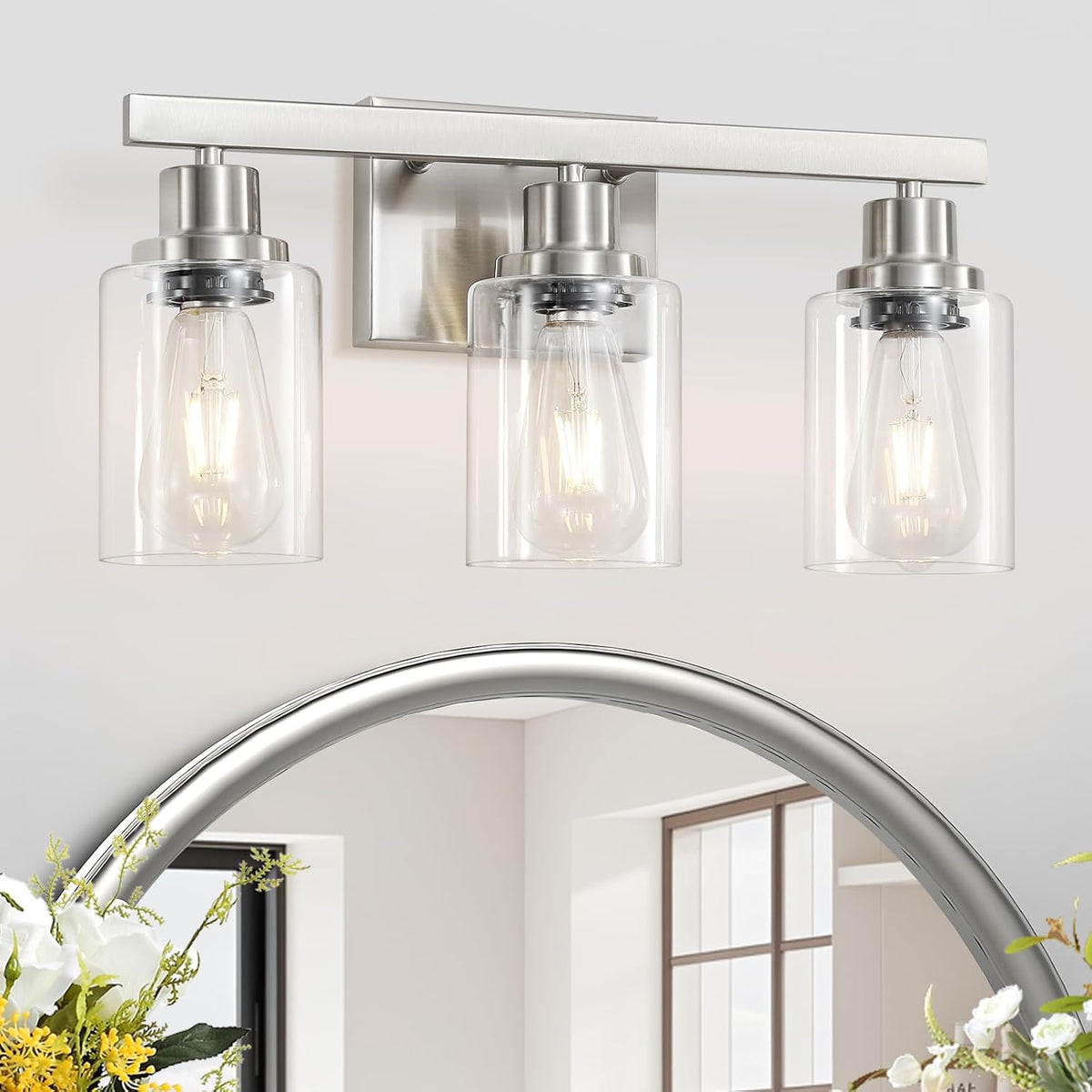 Three-light vanity fixture with clear cylindrical glass shades and brushed silver finish above a round mirror