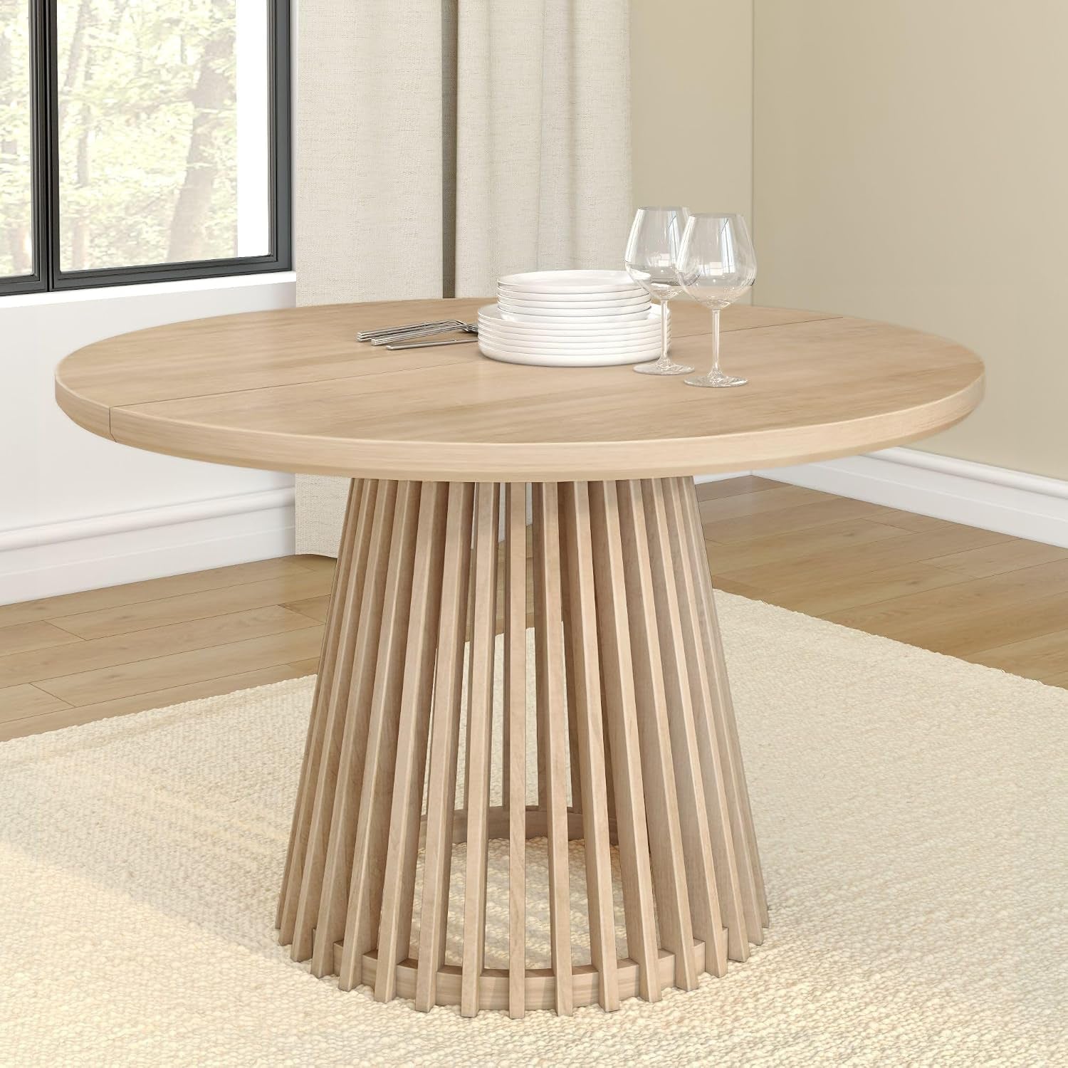 Round light-blonde wood dining table with vertical slatted pedestal displayed on a rug