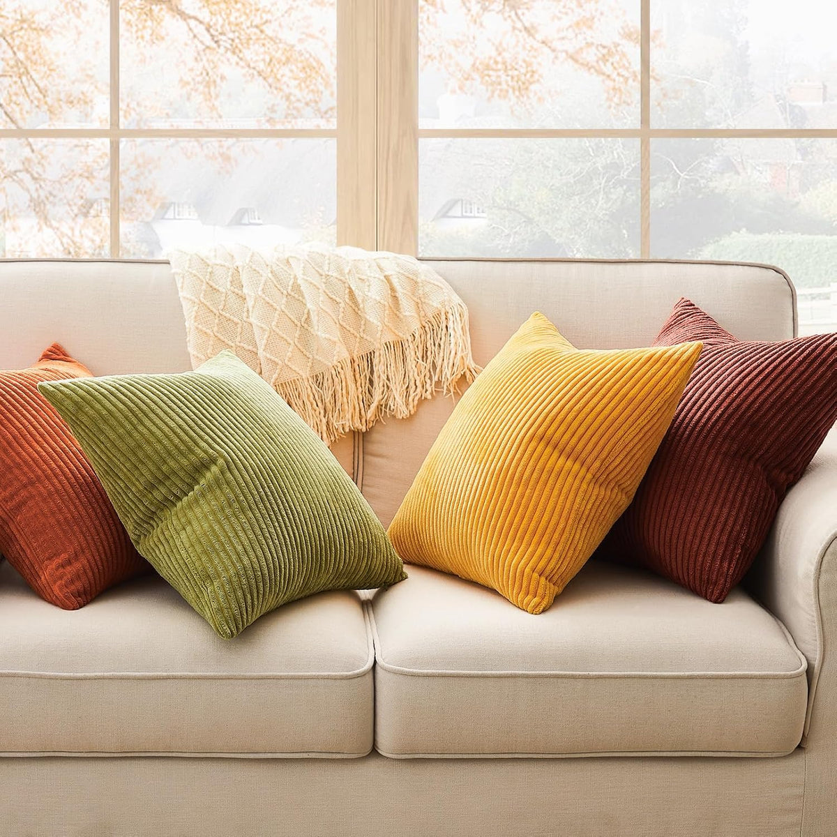 Assorted corduroy cushion covers in green, yellow and rust placed across a beige sofa with a knit throw