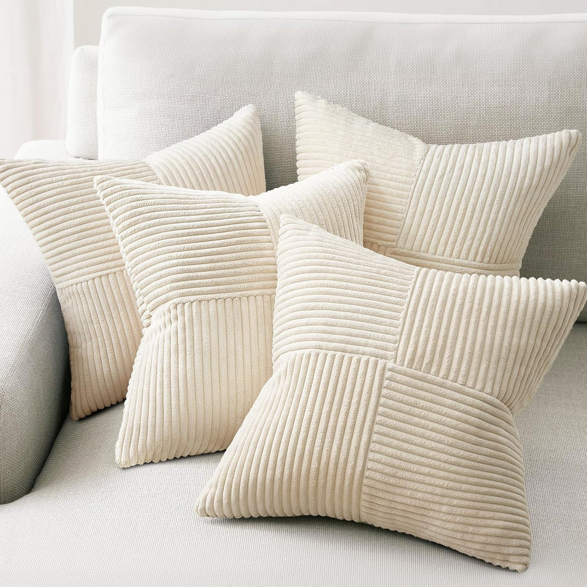 Four cream corduroy patchwork throw pillow covers arranged on a light sofa.