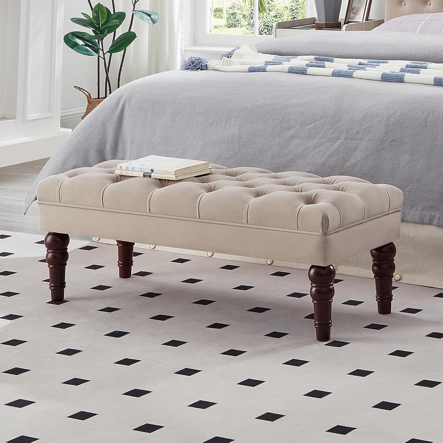 Beige tufted bench with turned legs and small caster wheels visible under the frame, books on top