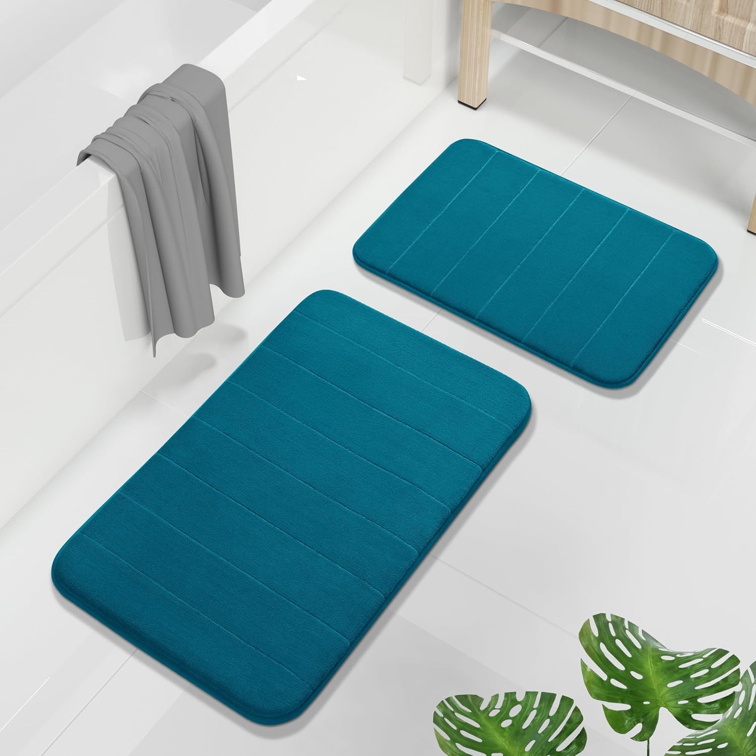 Two teal memory-foam bath mats on a glossy white floor beside a tub and wooden cabinet.