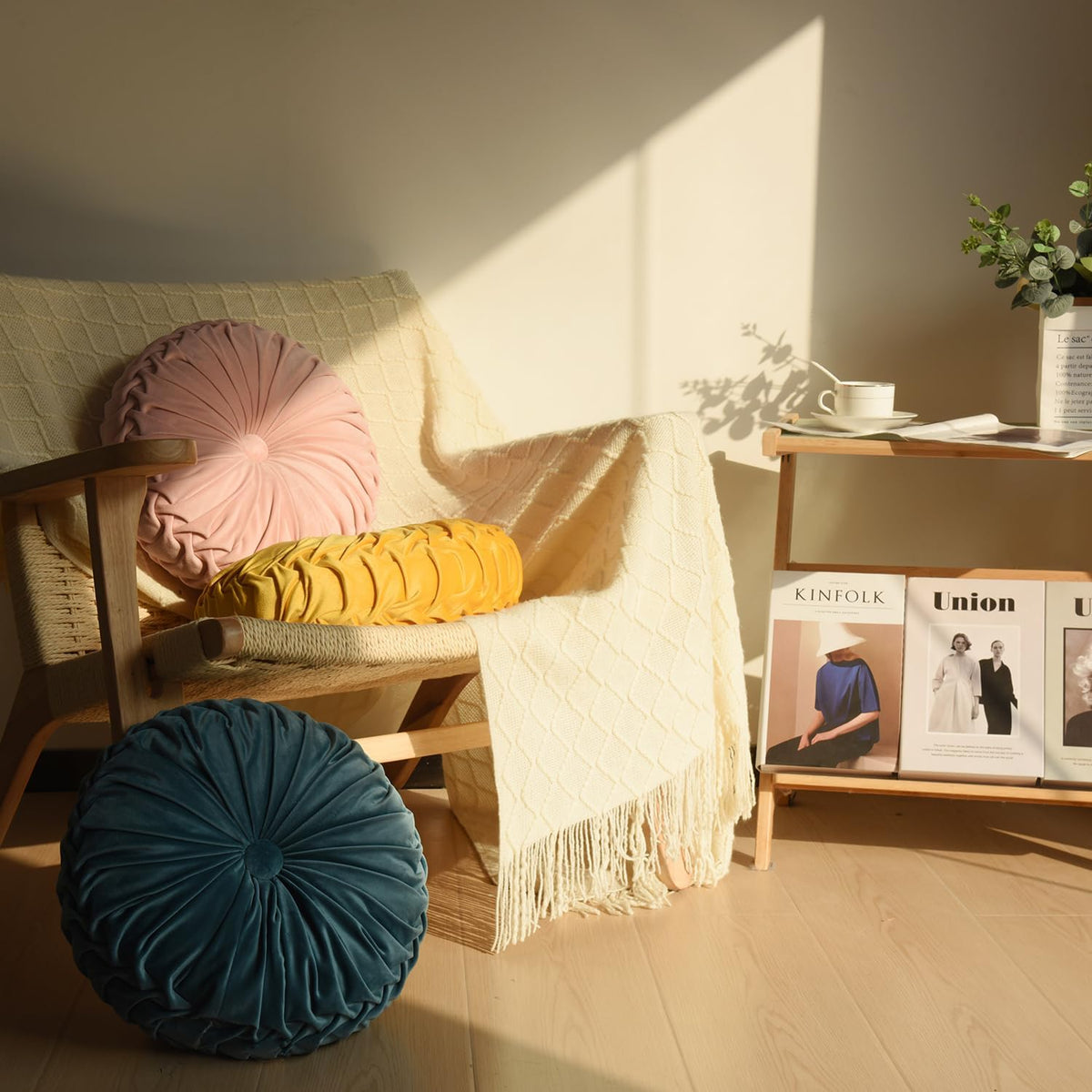 Interior scene with pink and yellow velvet ruched round pillows on a woven chair and a blue pillow on the floor