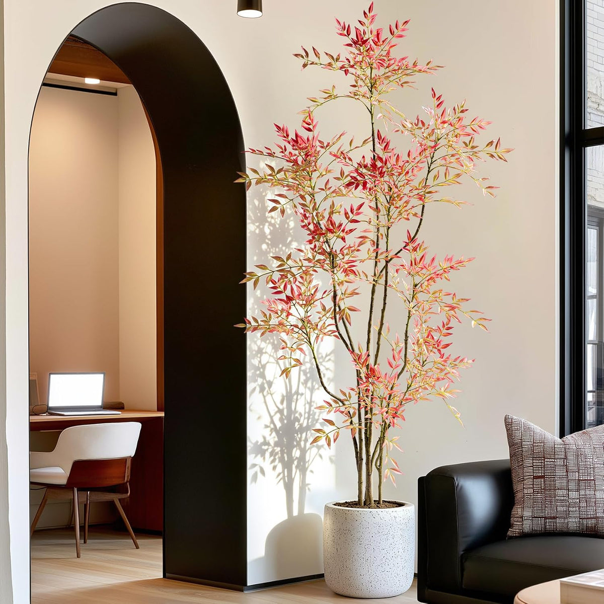 Faux Nandina with red-tipped foliage in a speckled white planter beside a black sofa and arched doorway