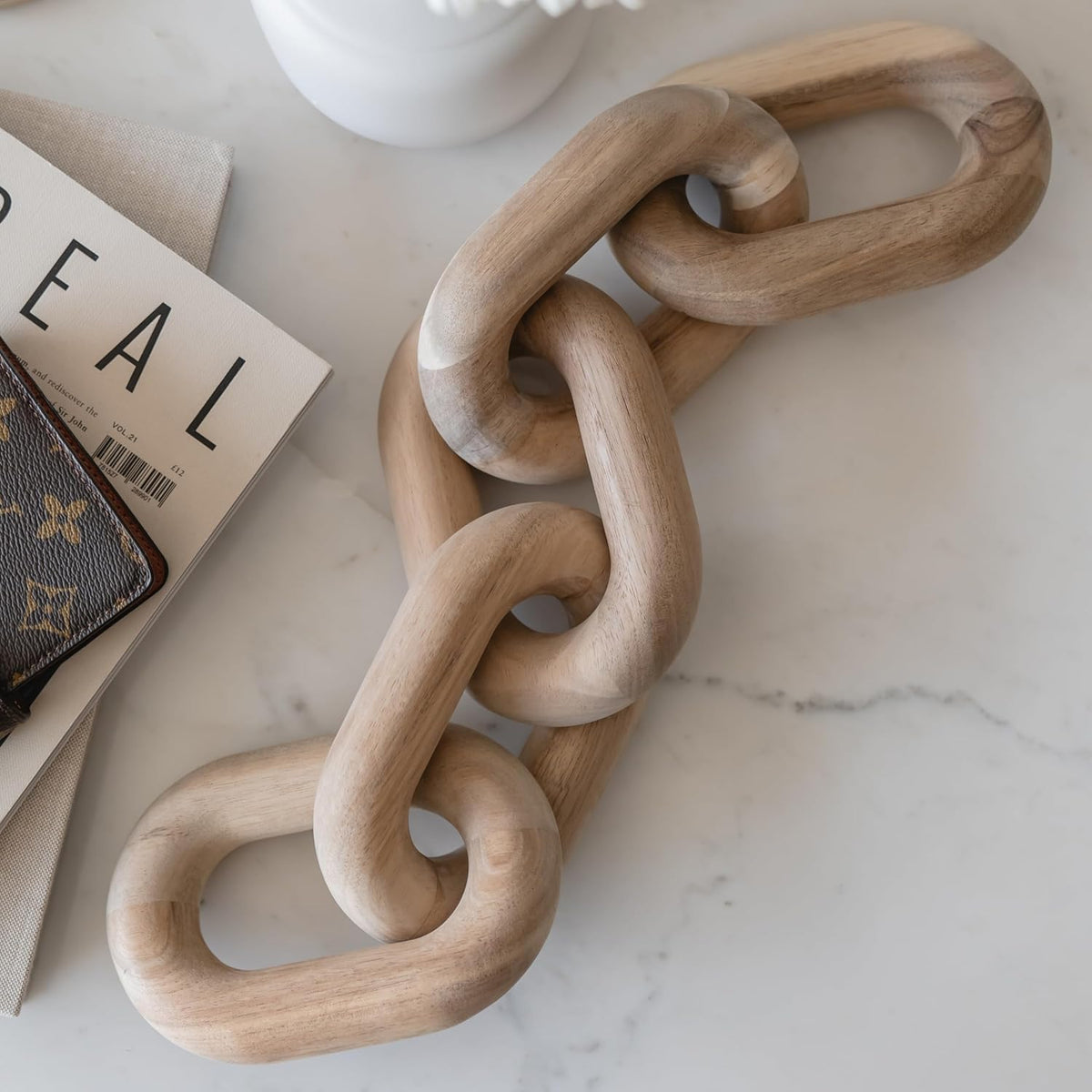 Hand-sanded acacia wood chain with matte finish, close-up angled on a marble tabletop beside a book.