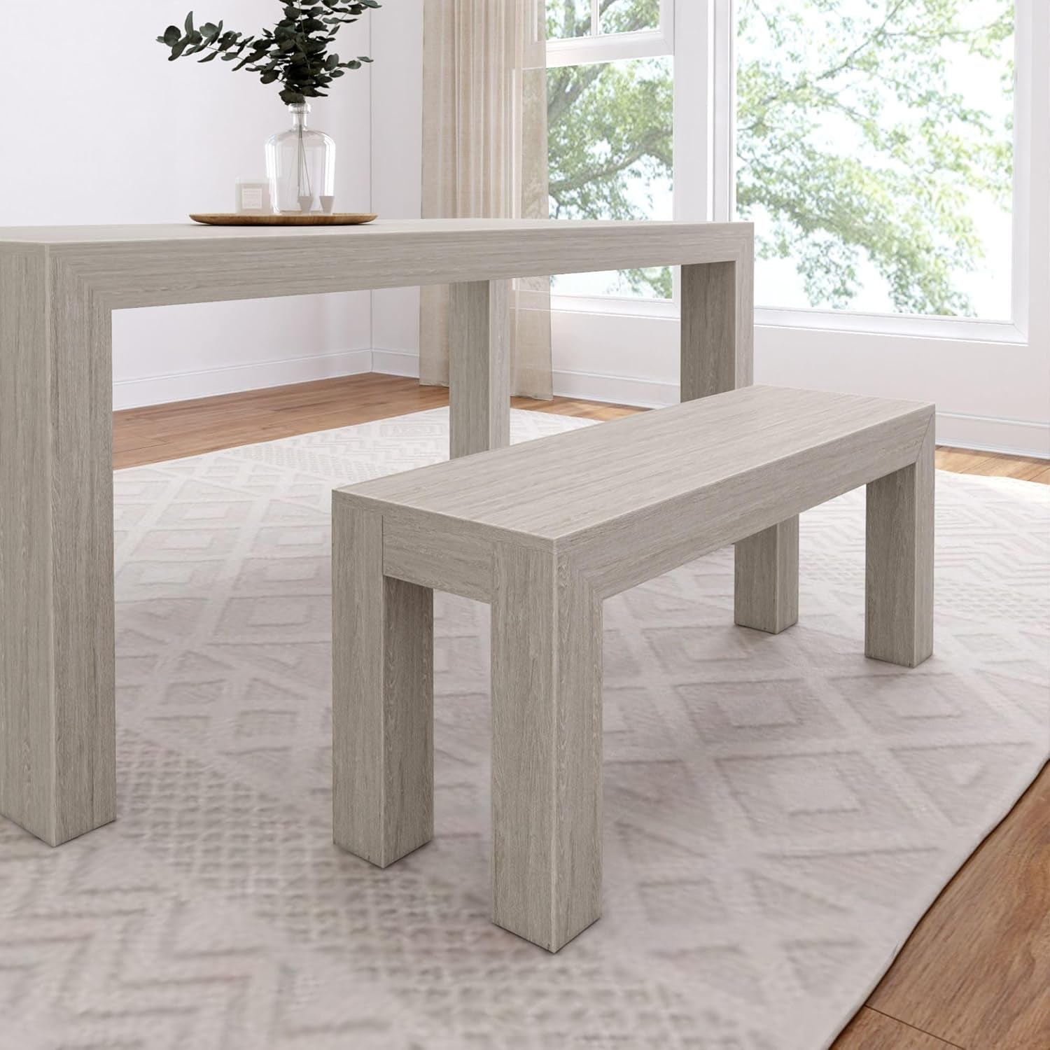 Closer side view of a matching rectangular table and bench in a pale gray wood finish on a rug