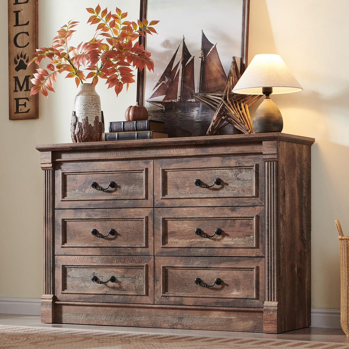 Front view of a wide weathered wood dresser with six drawers styled with lamps and decor on top.