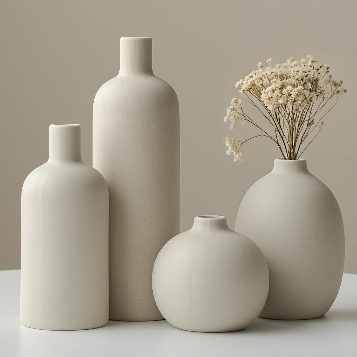Tight crop of four neutral vases highlighting subtle speckled finish and dried baby's-breath stems