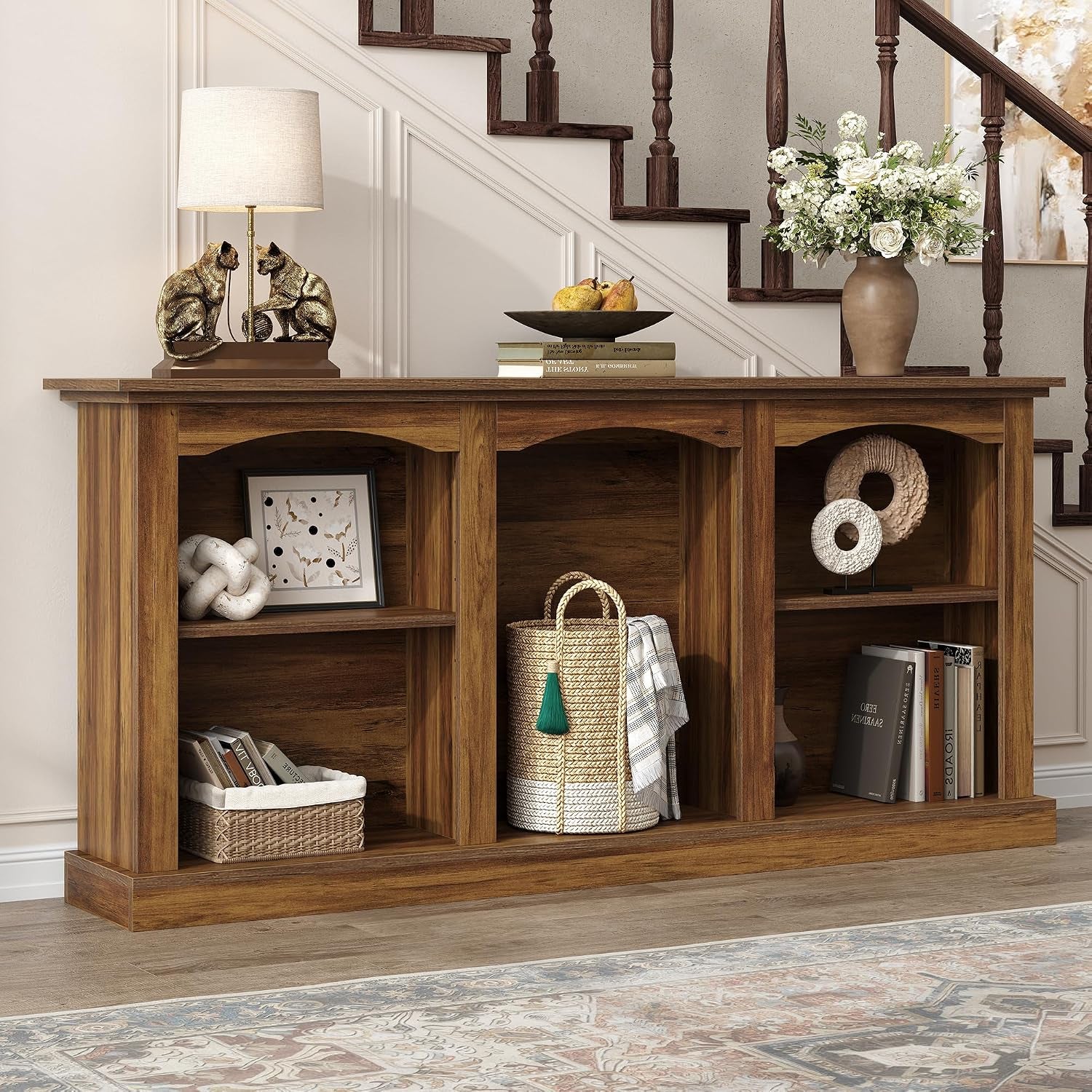 Angled view of the rustic console table placed near a staircase with baskets and books in the open compartments