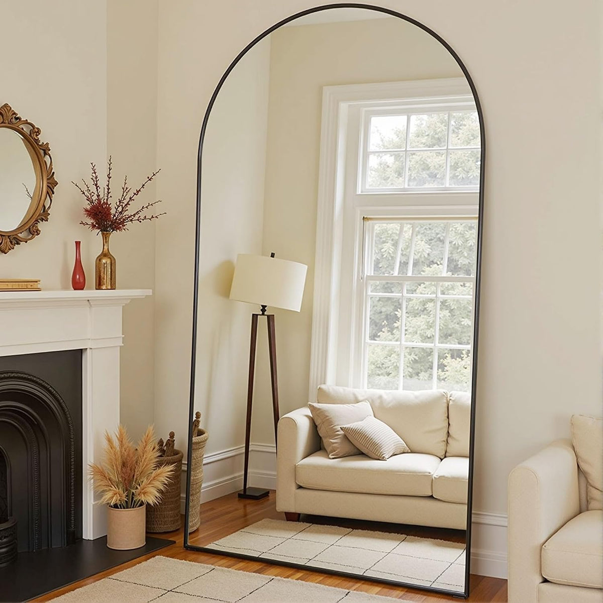 Tall arched floor mirror with thin black frame standing next to a sofa and floor lamp in a living room.