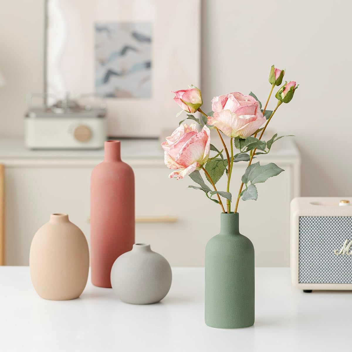 Grouped matte ceramic vases in muted green, terracotta, gray and beige on a dining table with room decor behind
