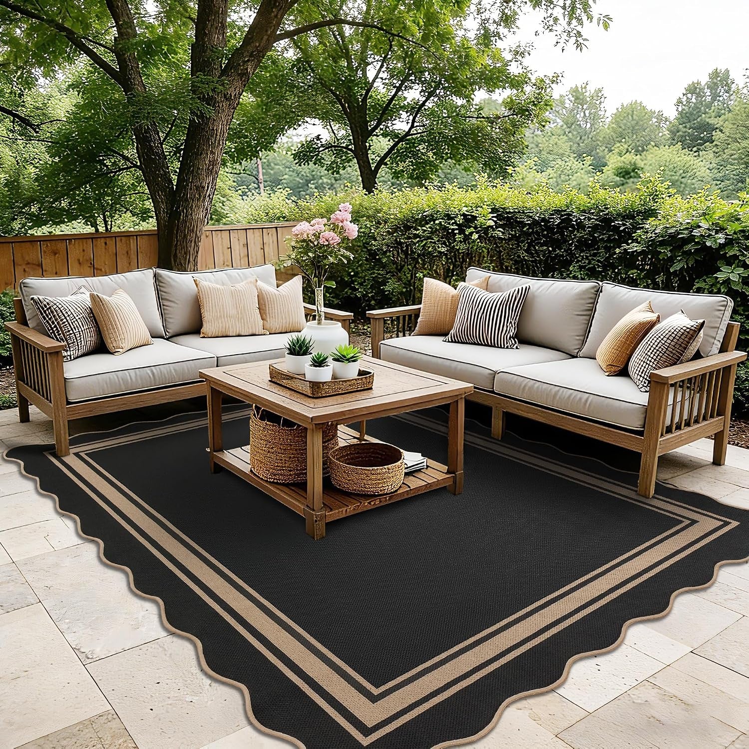 Black scalloped rug with tan trim beneath a wooden coffee table and two outdoor sofas in a garden patio.