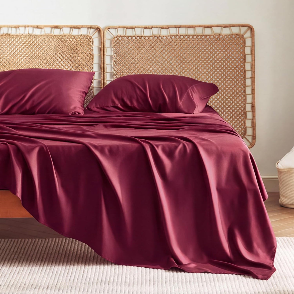 Deep burgundy sheet set on a bed with woven headboard and two matching pillows.