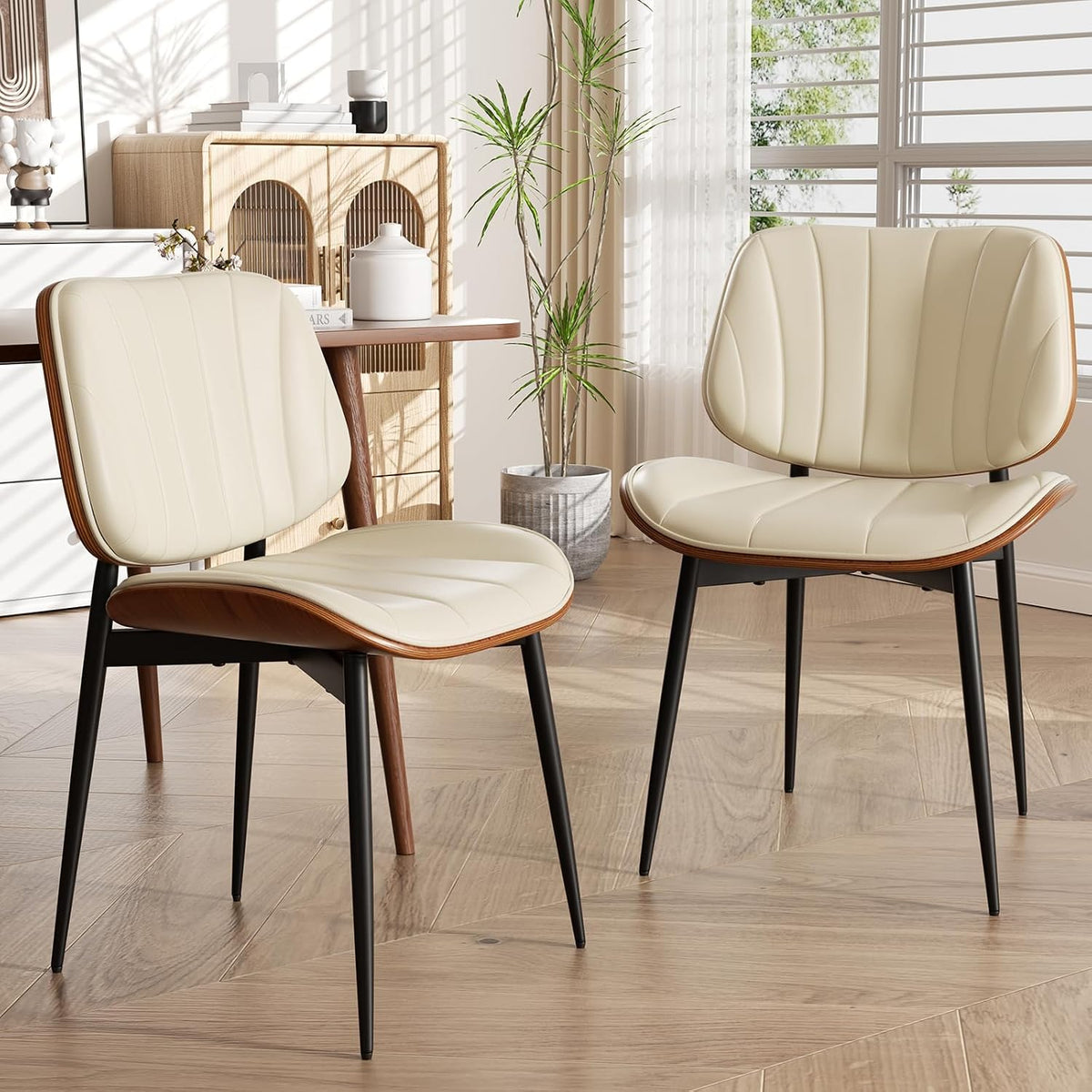 Two cream faux-leather dining chairs with walnut curved backs and black tapered legs beside a small cabinet.