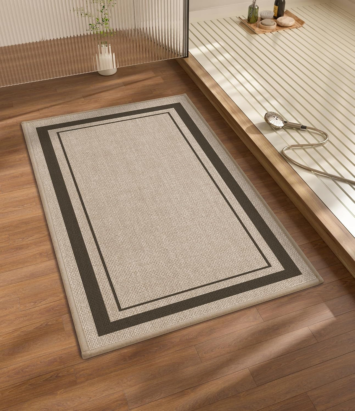 Beige bath mat with textured surface and two dark border lines on a wood floor next to a slatted shower platform.