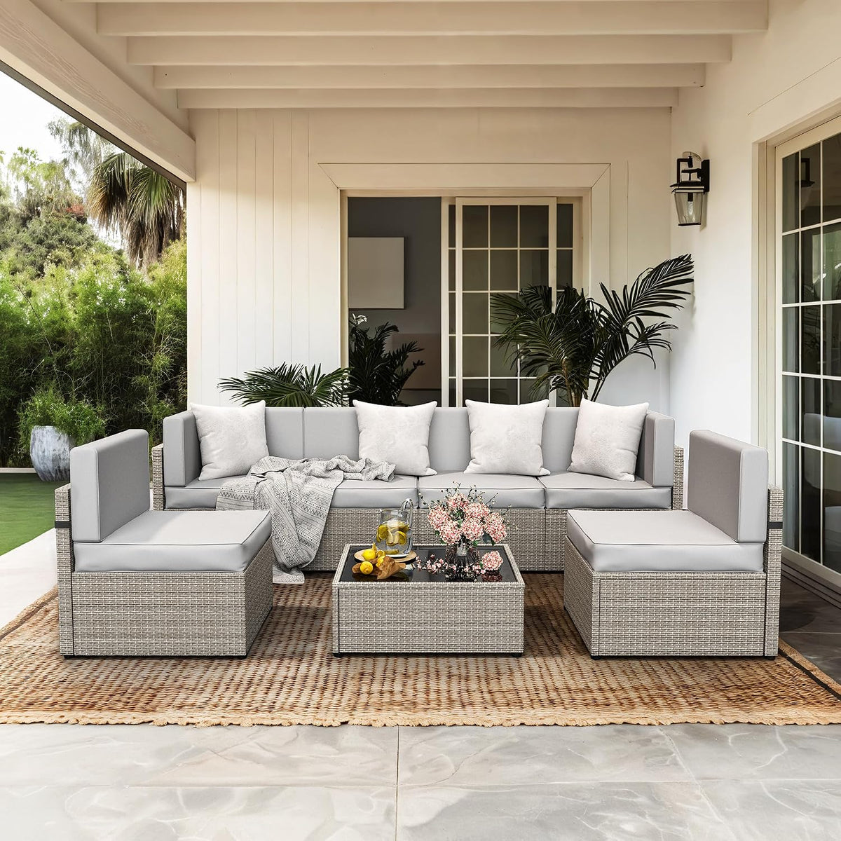 Outdoor covered patio with a light gray wicker 7-piece sectional, matching coffee table, cushions on a woven rug