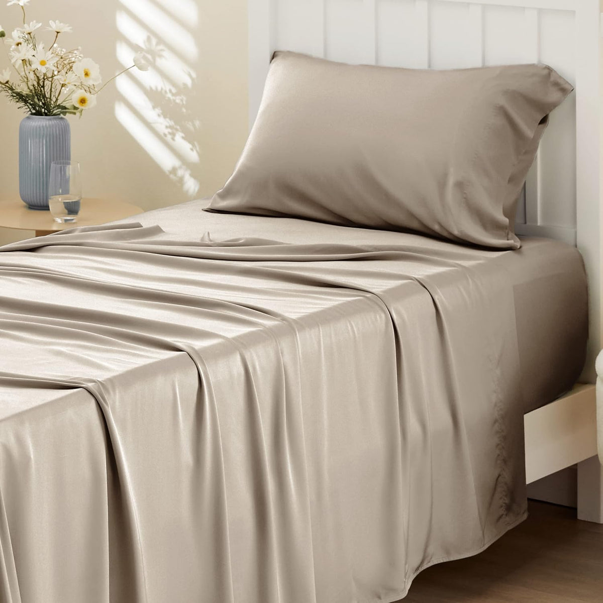Side view of a single bed with draped taupe satin-like sheet and matching pillow against a white slatted headboard.