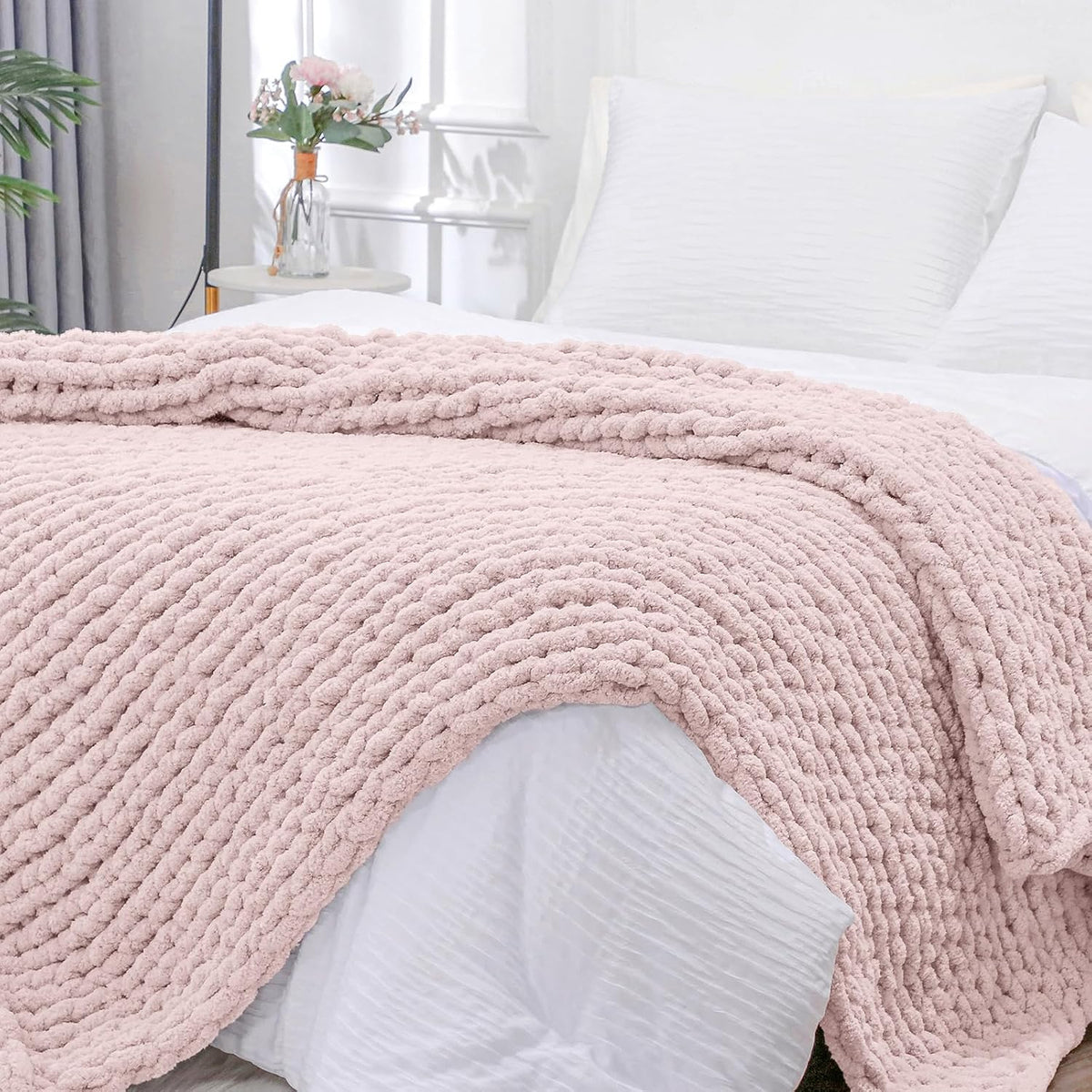 Close-up of a chunky ribbed knit throw draped over the foot of a bed in a soft pink-beige tone
