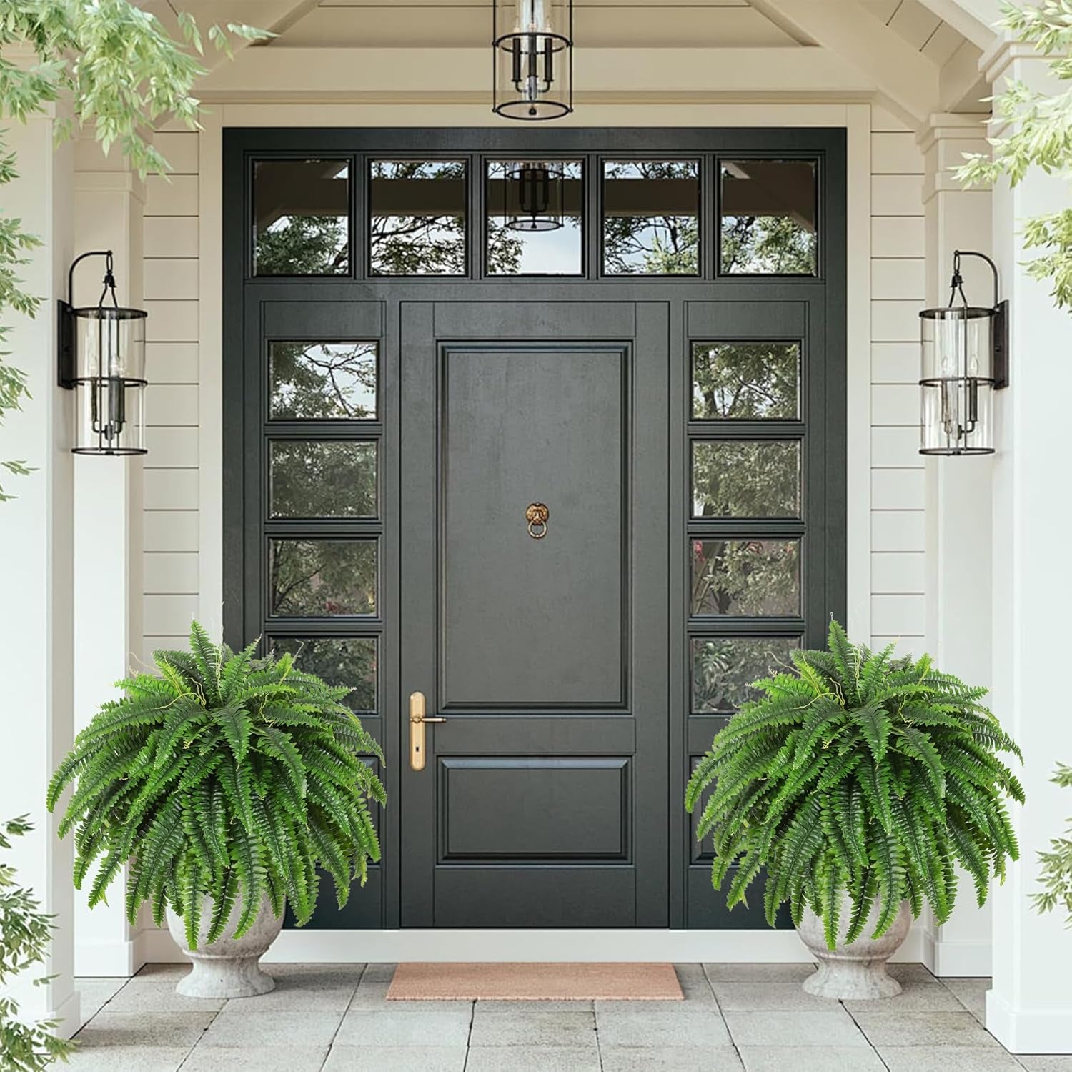 Two green artificial Boston fern bushes in stone planters flanking a black front door