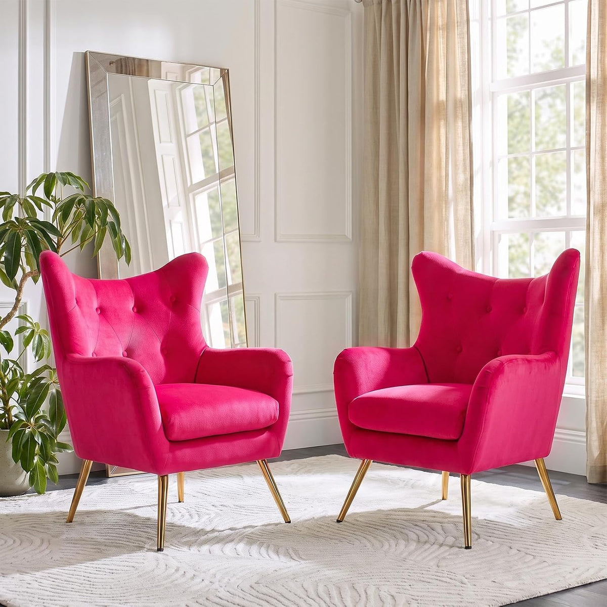Pair of bright fuchsia wingback chairs arranged side by side in a sunlit room with a large leaning mirror.