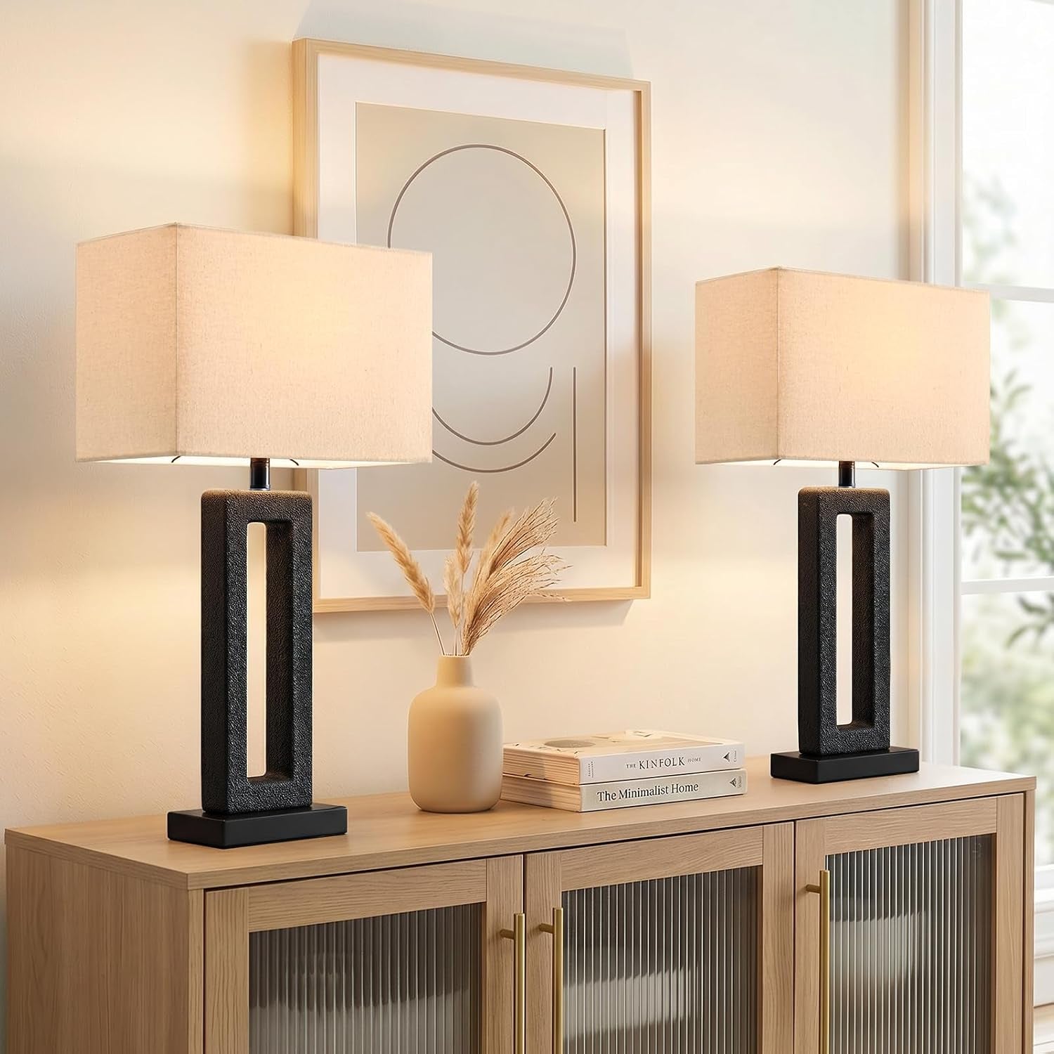 Pair of black textured rectangular table lamps with beige rectangular shades flanking framed art on a sideboard