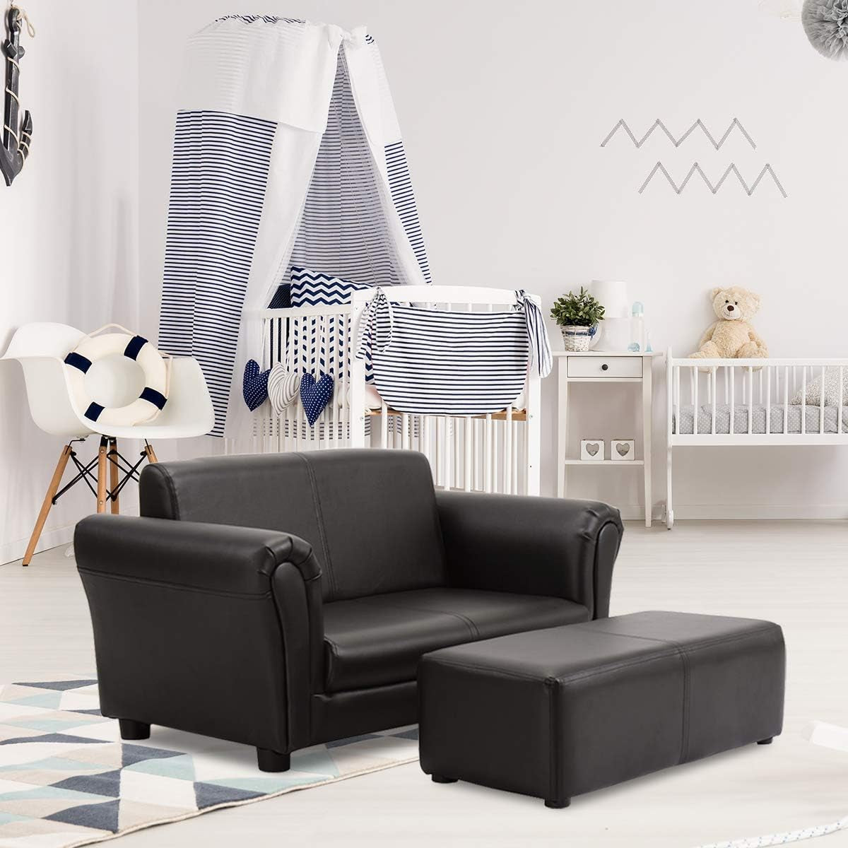Black loveseat and matching ottoman staged on a rug in a bright nursery-style room with crib and chair behind.
