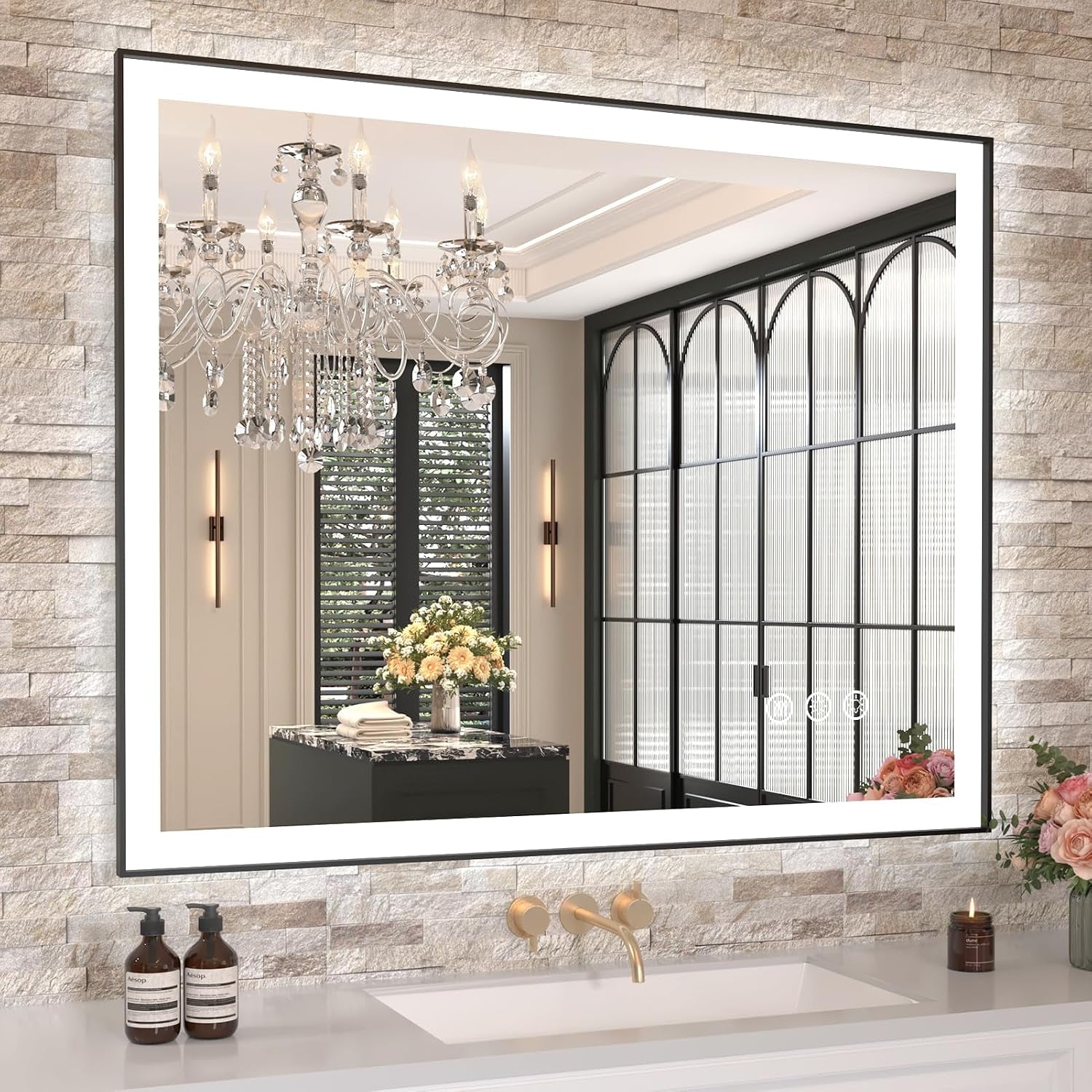 Large rectangular LED mirror on textured stone wall reflecting a chandelier and arched window panels.