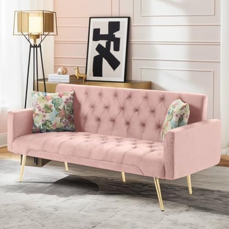 Pink velvet sofa upright with tufted back, slim gold legs and two floral pillows.