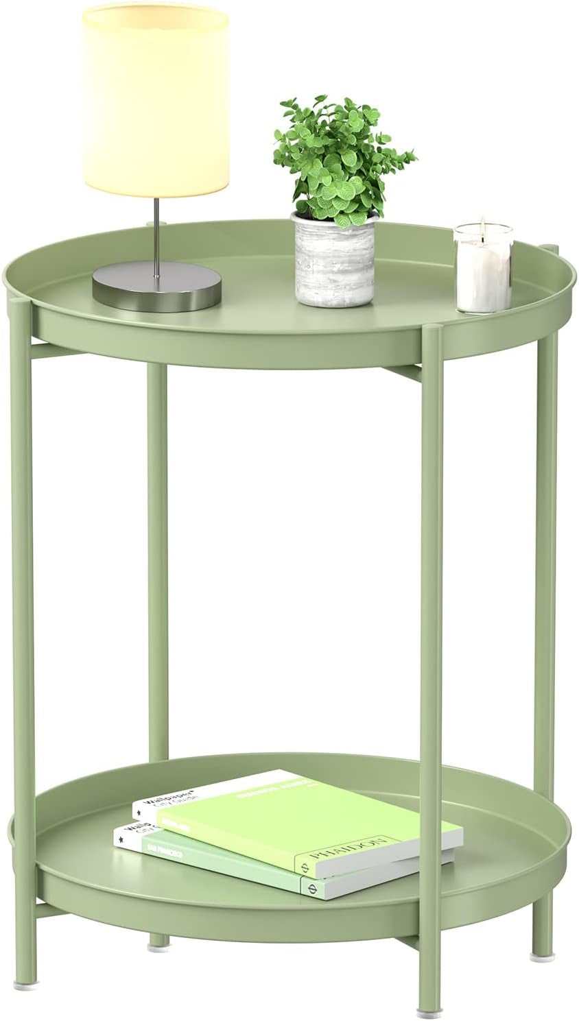 Studio close-up of a green two-tier round metal side table with a lamp, small plant, candle, and books.