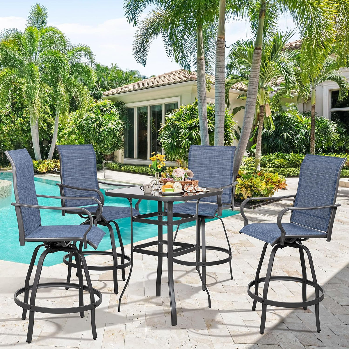 Wide view of the set in blue fabric showing four chairs around the glass-top table beside a tropical pool.