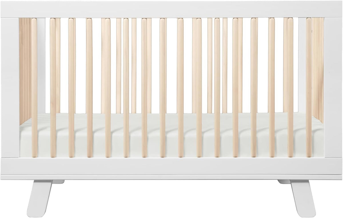 Front view of a white-framed crib with natural wood slats and a mattress inside.