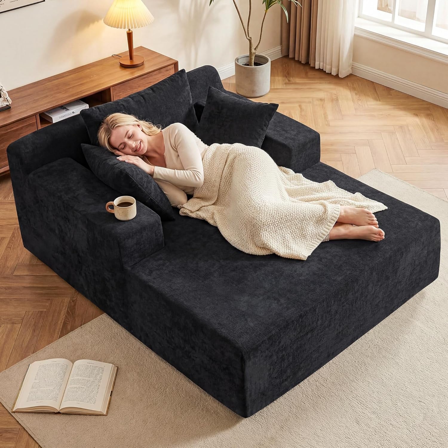Top-angled view of a very dark charcoal boneless chaise with three matching pillows and a woman reclining under a cream