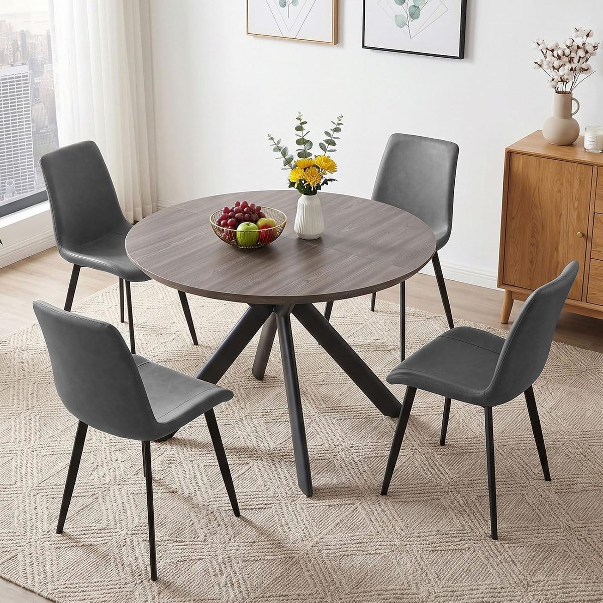Round dark wood table with four gray chairs on a patterned rug by a sideboard and window.