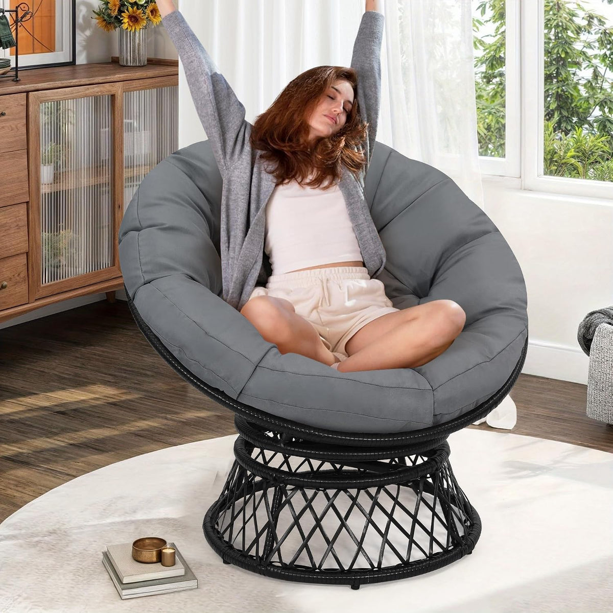 Front view of a gray-cushioned papasan chair with a woman stretching inside in a bright room.