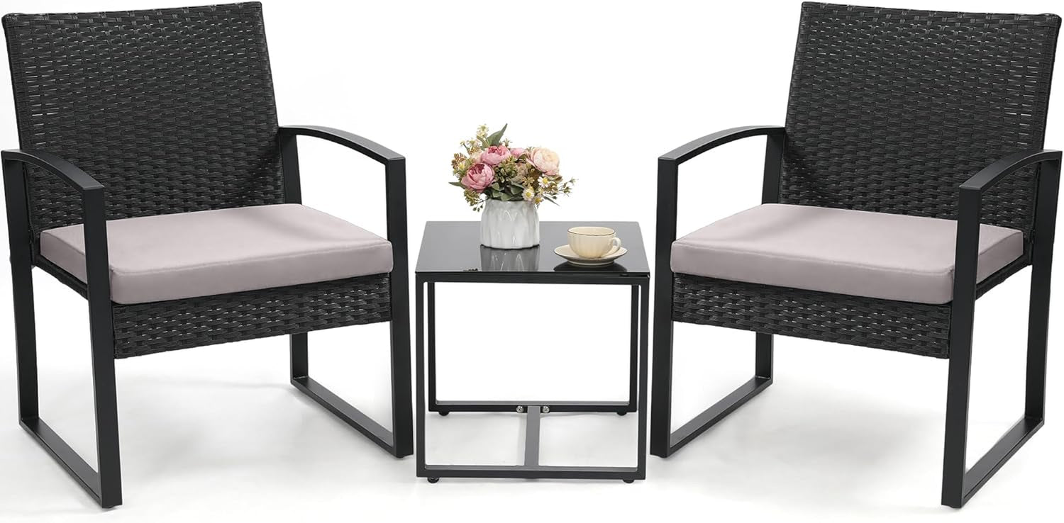 Two black-rattan armchairs with light gray seat cushions and a small black glass-top side table with flowers