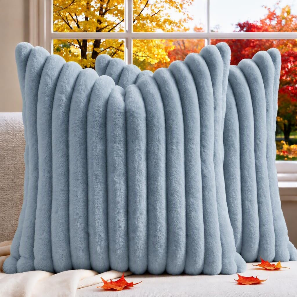 Pair of ribbed faux-fur throw pillows in pale blue sitting on a couch with autumn leaves outside a window.
