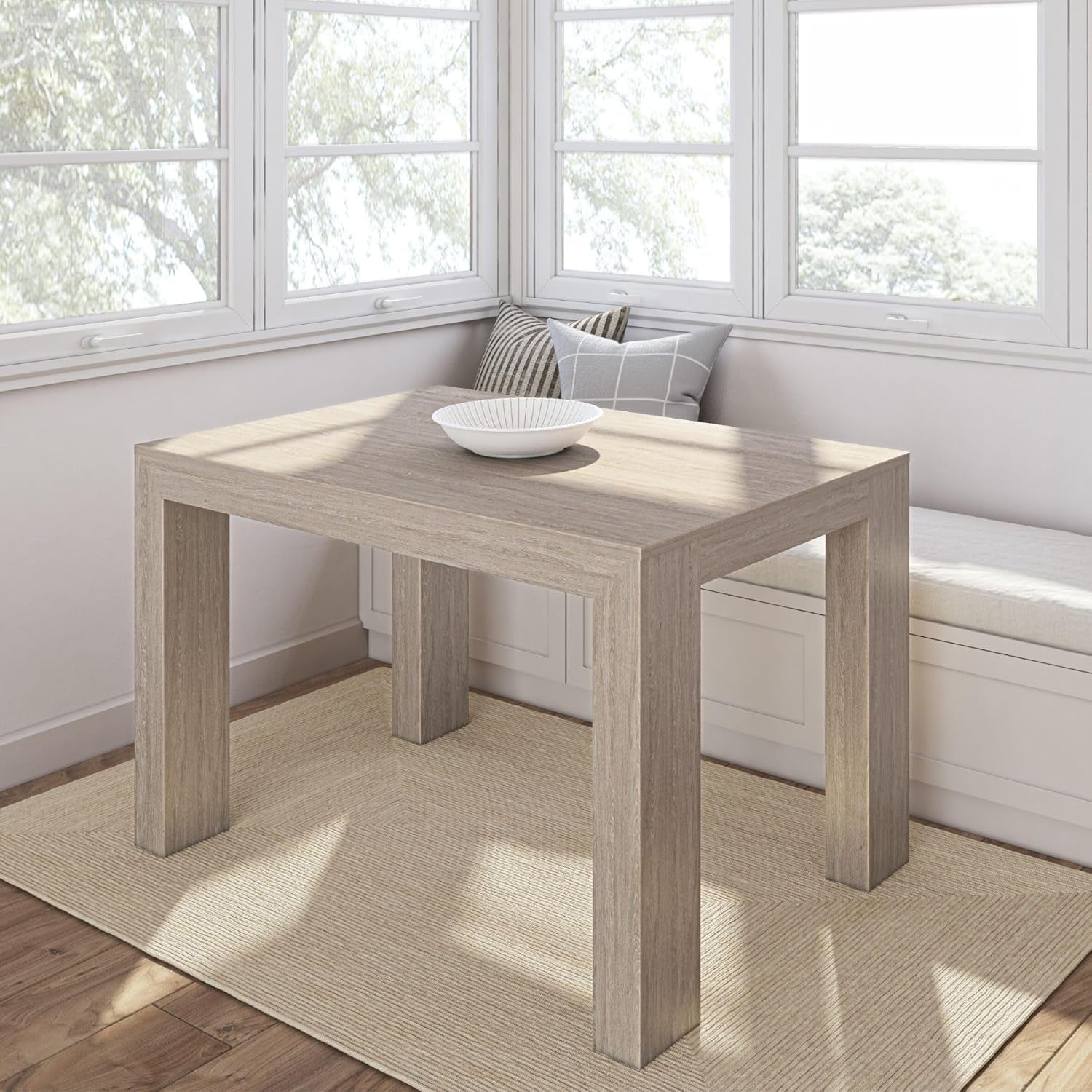 Small square pine table in a sunlit window nook with bench cushion and decorative pillows