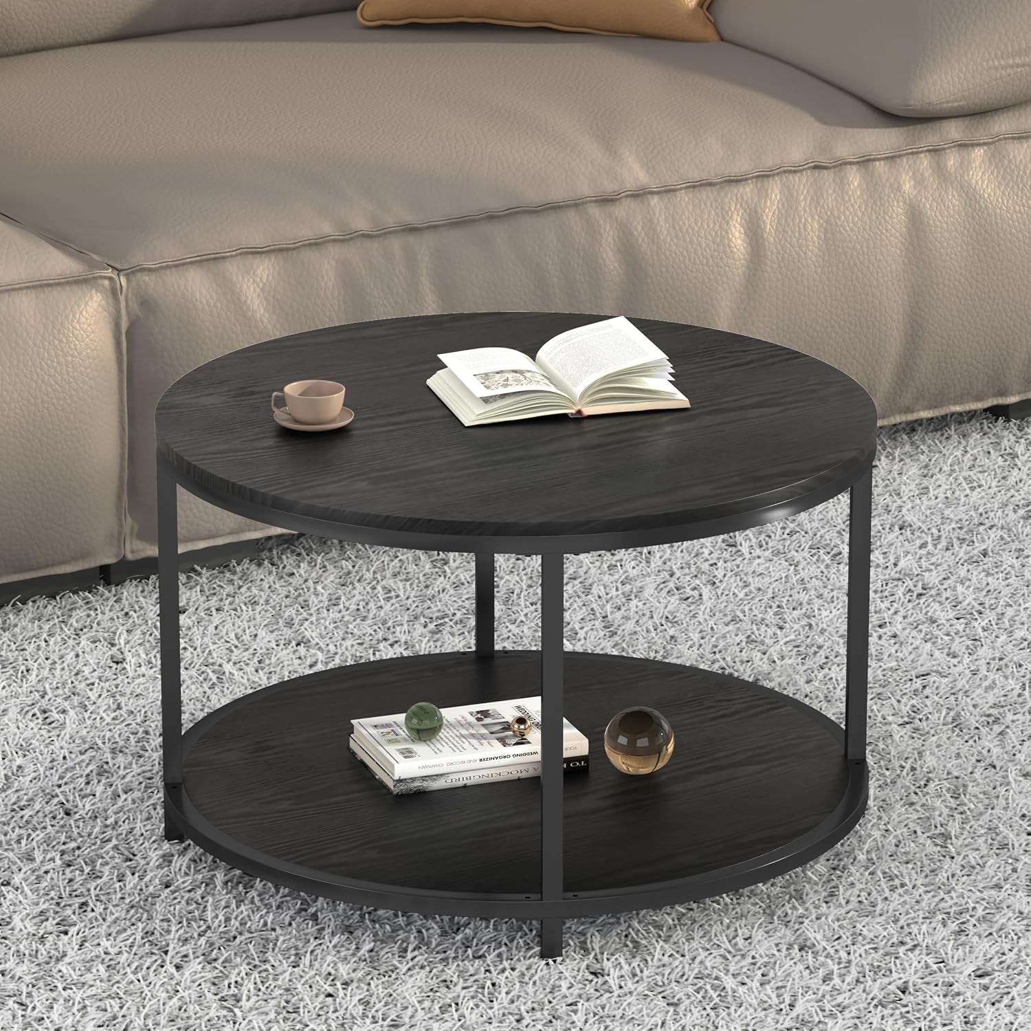 Round two-tier coffee table in dark finish with book and cup on top beside a beige sofa