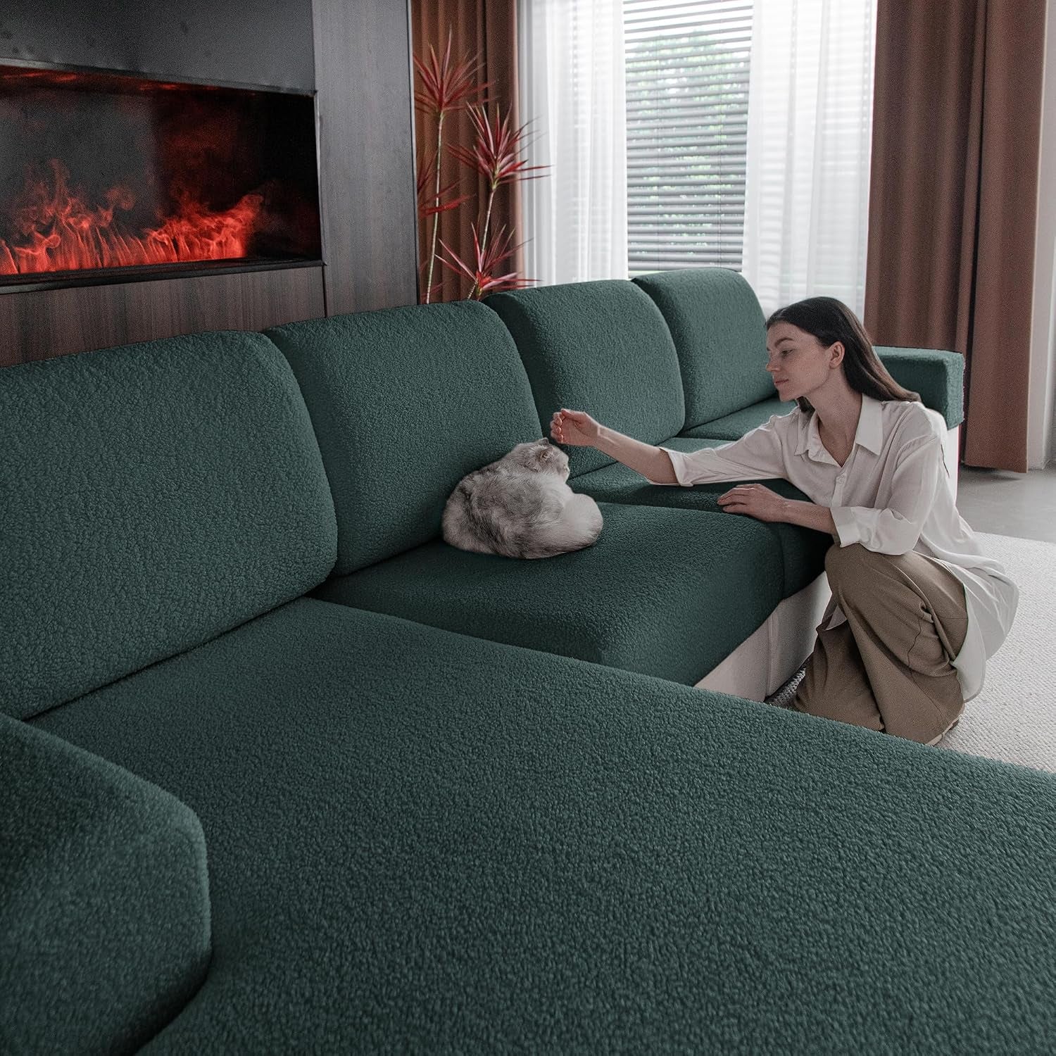 Deep green sectional slipcovers with a woman kneeling to pet a cat curled on the seat.