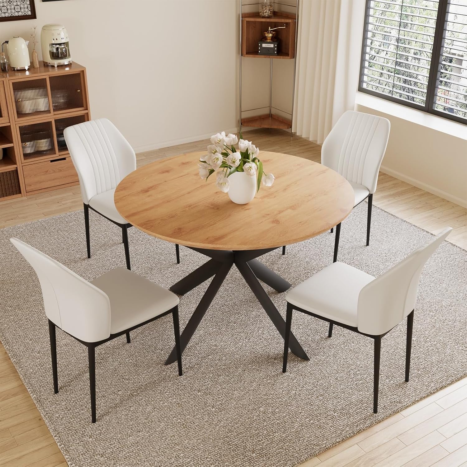 Round light-wood table with four white chairs arranged on a textured rug.