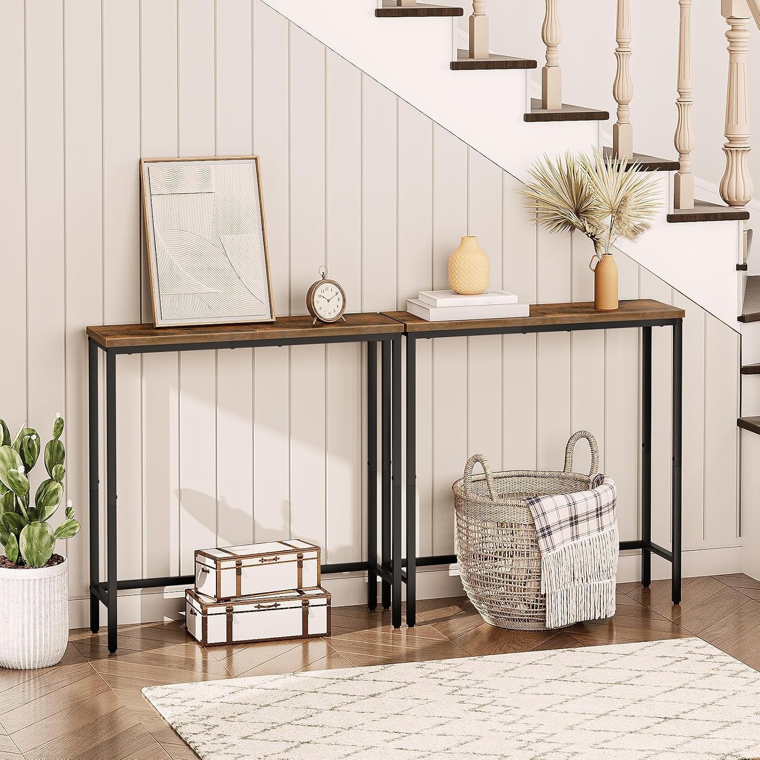 Two narrow console tables with rustic tops and black frames styled beneath a staircase with baskets and decor.