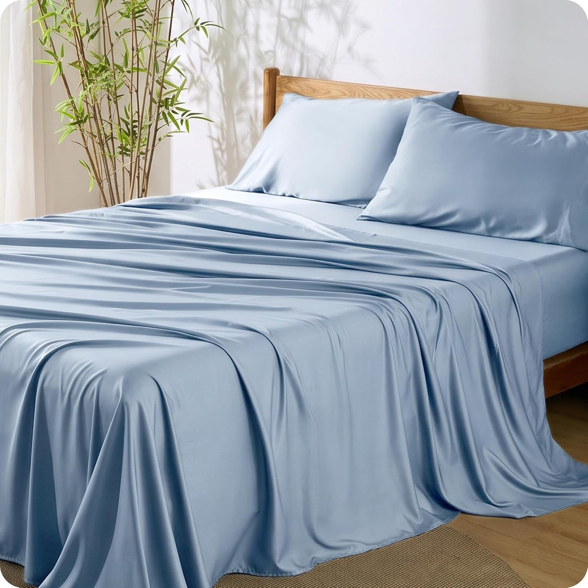Pale blue sheets and matching pillowcases on a wooden bed with a tall plant casting shadows.