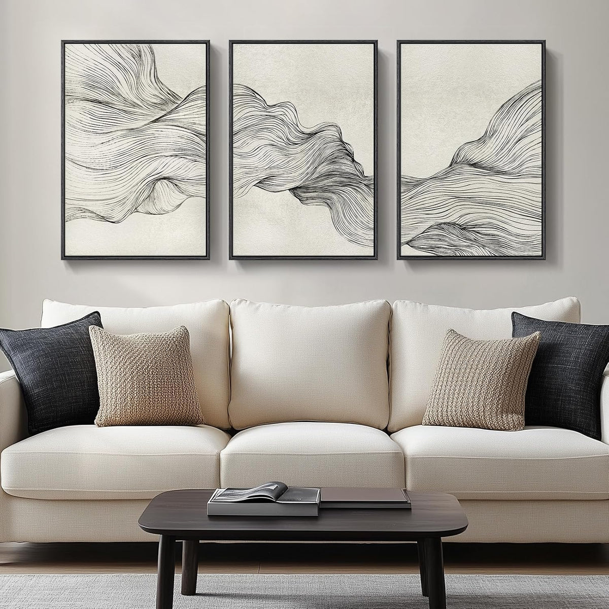 Three vertical framed panels with flowing black line abstract on cream hung above a beige sofa with pillows.