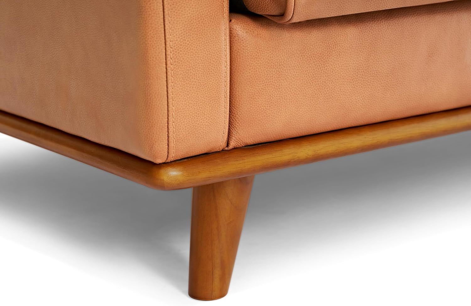 Close-up of the sofa's wooden tapered leg and base trim beneath cognac leather upholstery.