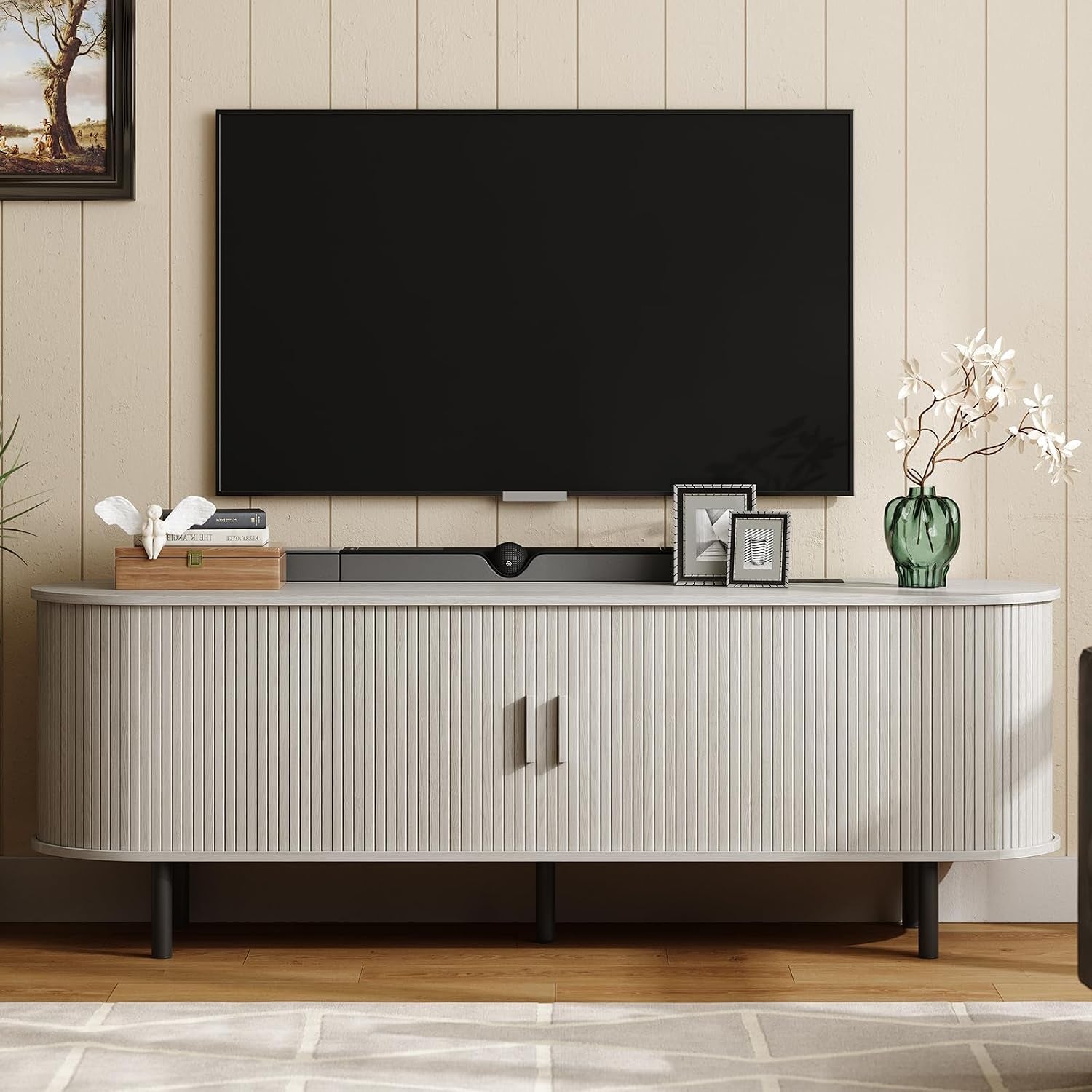 Front-facing view of the TV stand in a light gray finish beneath a wall-mounted TV with decorative vases.