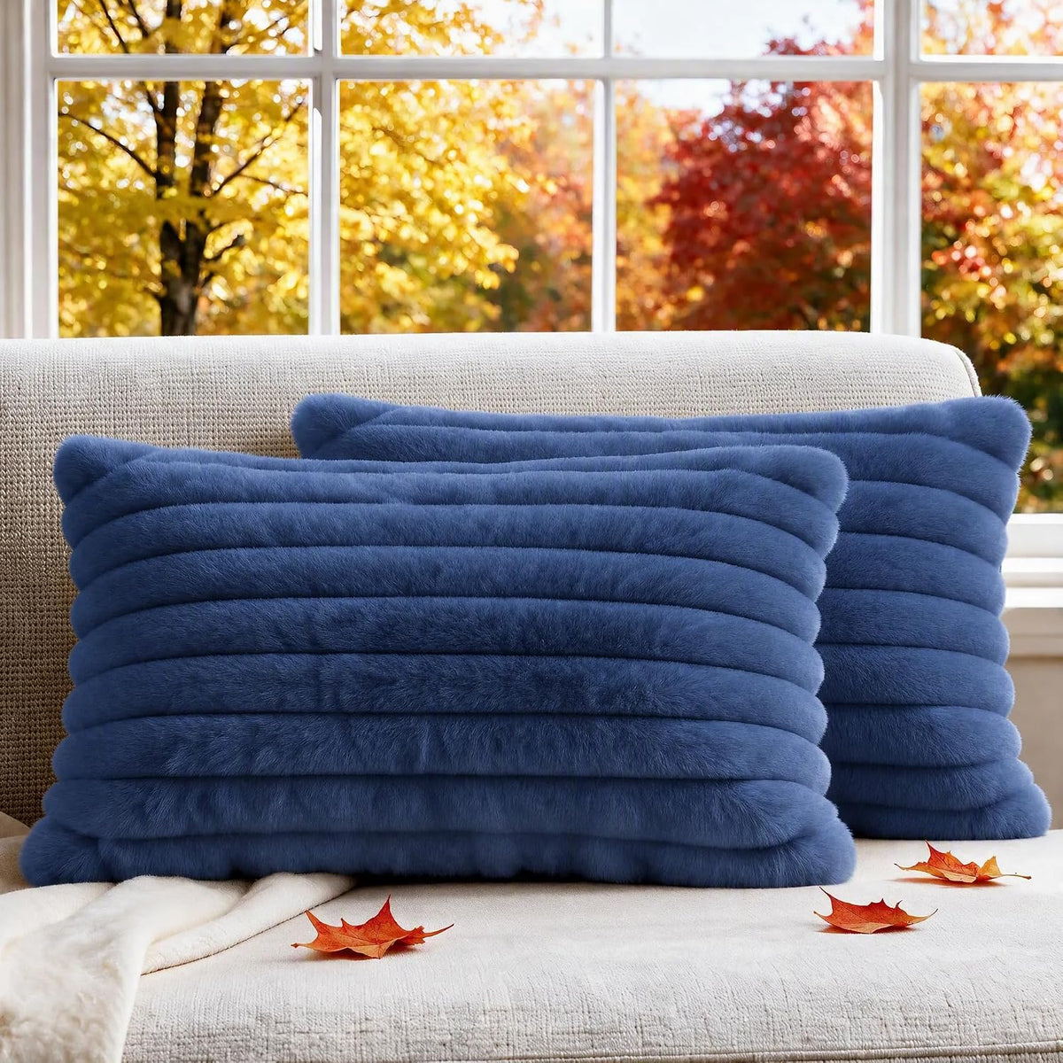 Two deep blue ribbed faux-fur rectangular pillow covers staged on a beige sofa with fall leaves and a window in the