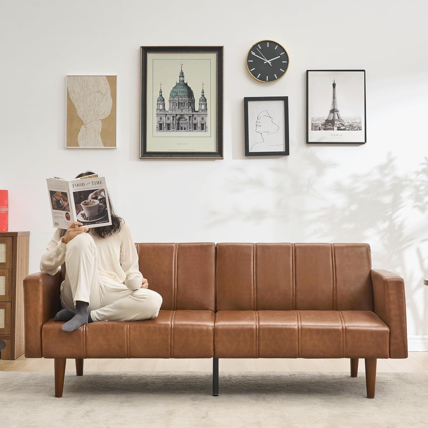 Straight-on view of person sitting cross-legged on brown PU leather futon sofa in a living room setting