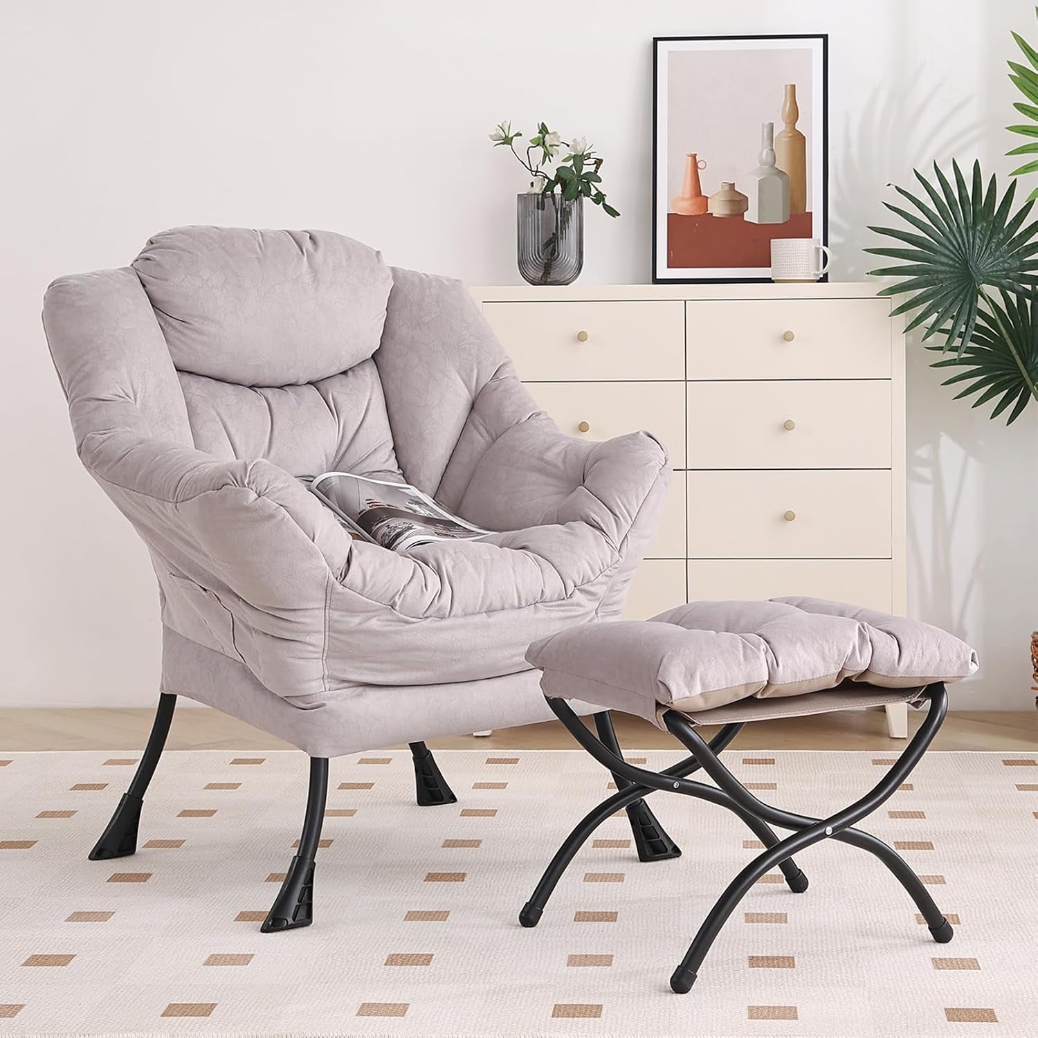 Light gray cushioned armchair with matching ottoman in a styled room with dresser and plant.